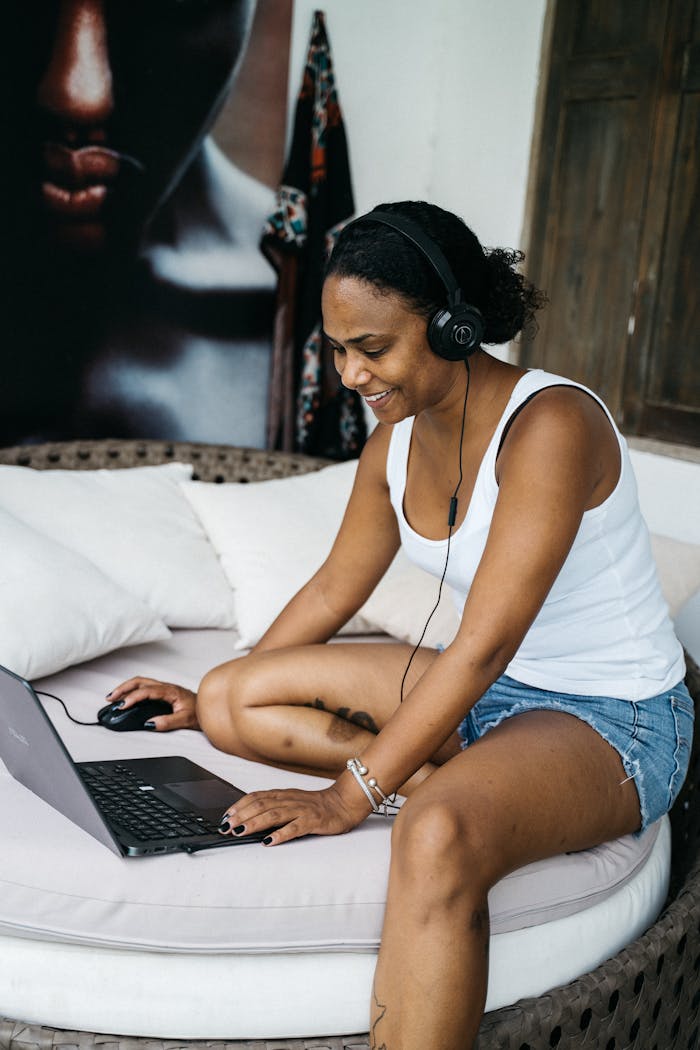 African American woman working remotely from home, using a laptop and headphones, seated comfortably indoors.