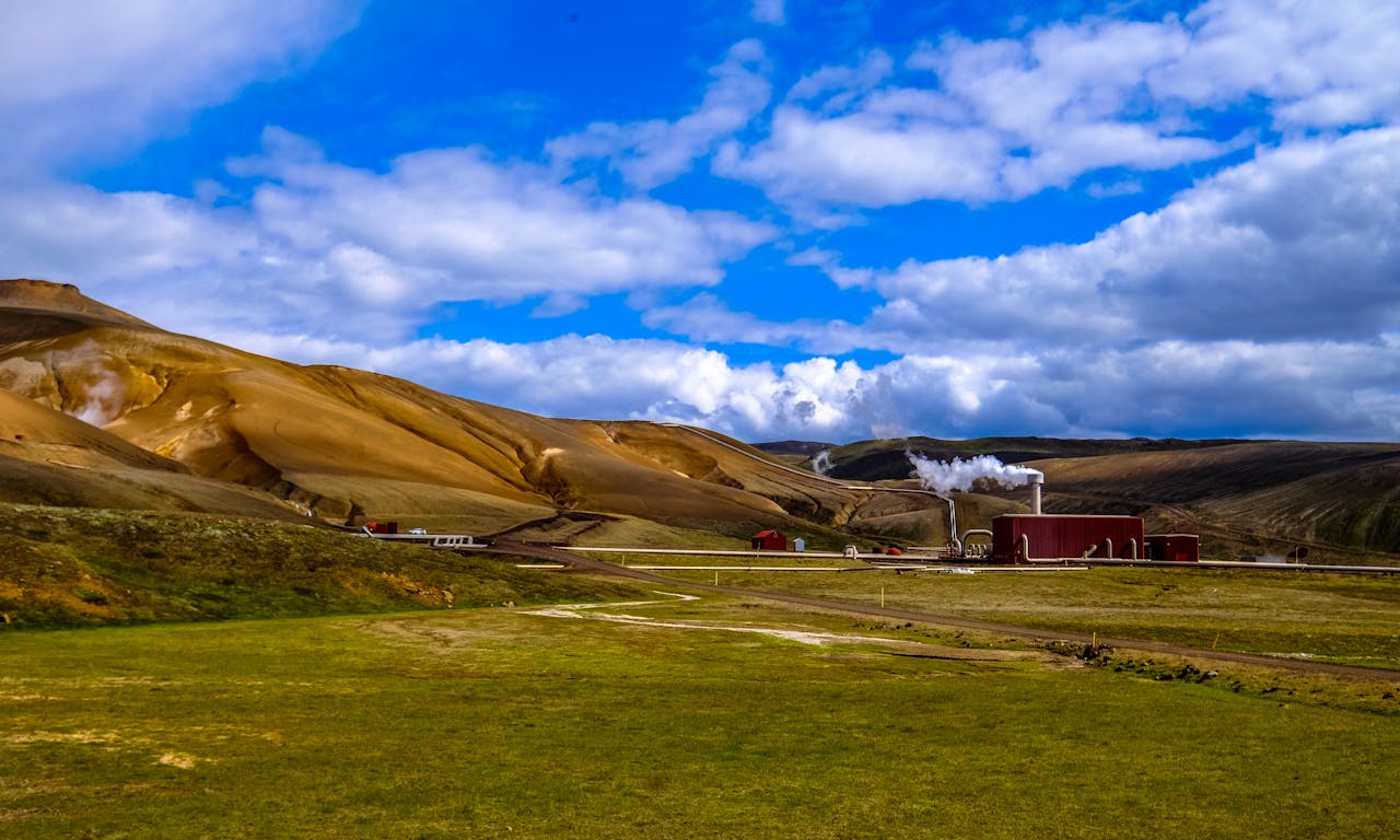 Beautiful countryside landscape with a factory and smoke against a backdrop of rolling hills and blue sky.
